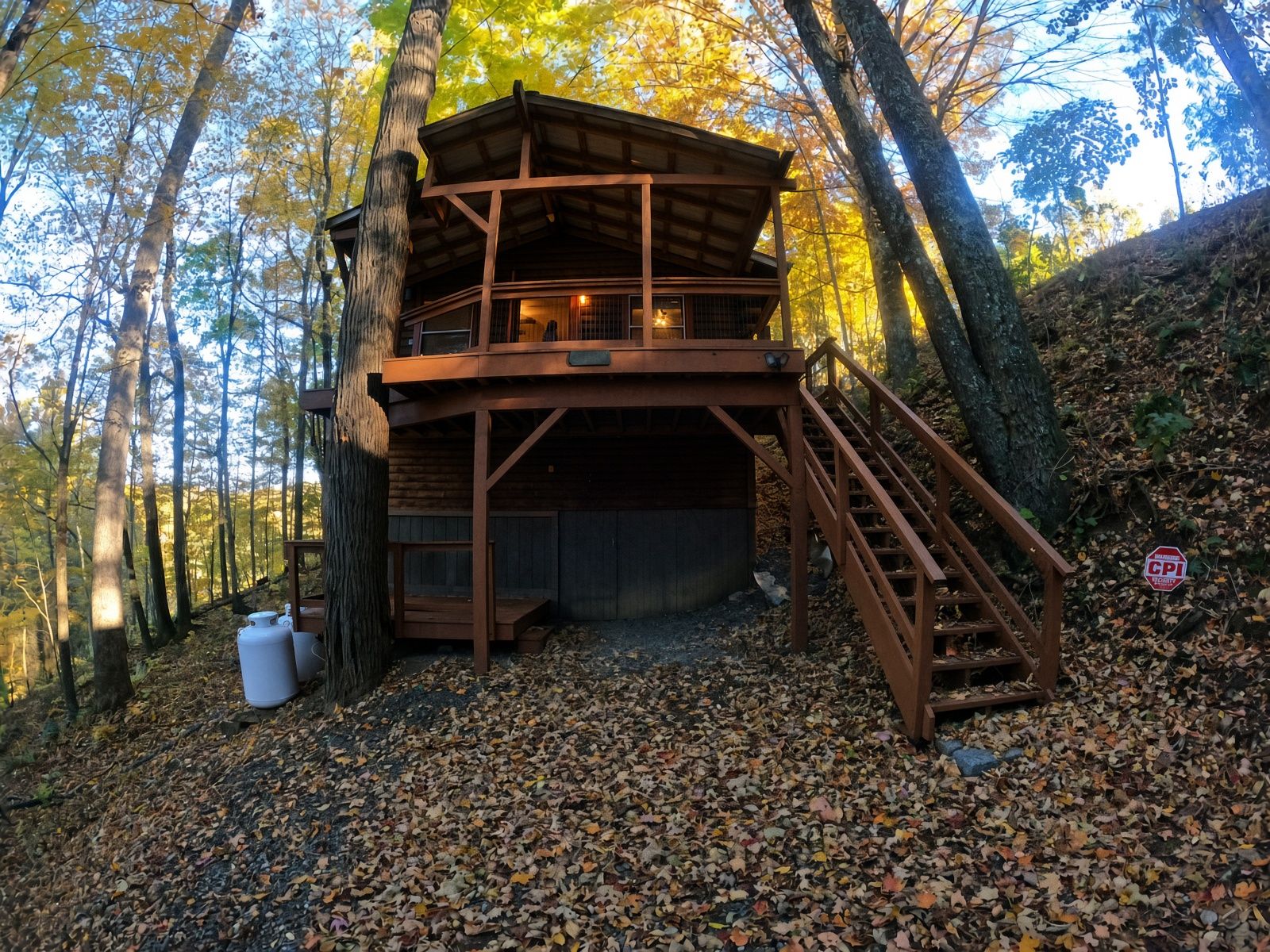 Eine Holzhütte mit Balkon und Treppe, umgeben von Bäumen und herabgefallenen Blättern.