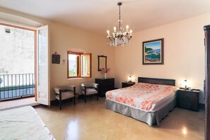 Un dormitorio con cama, dos sillas, cómoda, mesita de noche, candelabro, ventana y un cuadro.