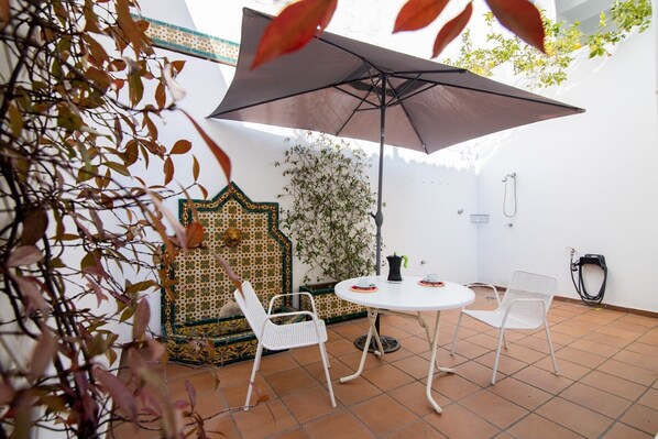 Un patio con mesa y sillas, un muro decorado y una ducha colgante.