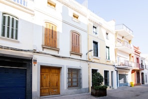 Una hilera de edificios blancos con contraventanas de madera, una puerta de garaje azul y una pequeña planta en maceta en la acera.