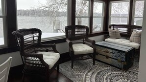 A cozy room with wicker chairs and a cushioned bench by large windows overlooking a body of water.