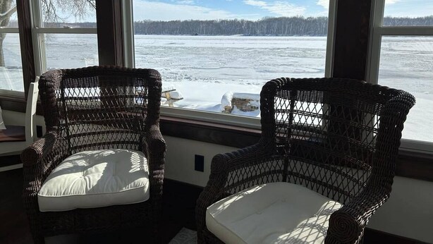 Two wicker chairs with cushions facing a large window with a view of a snowy landscape.