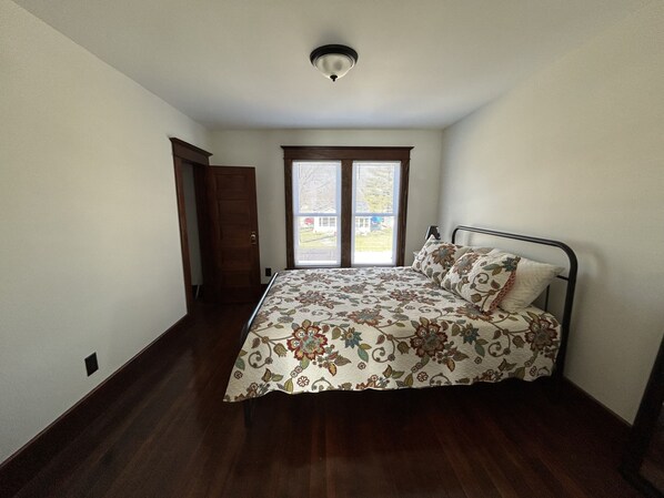 A bedroom with a bed, a window with blinds, a door, and a ceiling light fixture.
