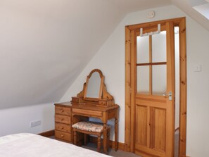 A bedroom with a wooden dresser, a mirror, a bed, and a door. - Sycamore Cottage - UK45923 (Ballater)