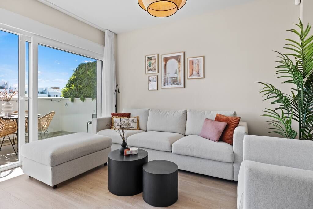 Un salon moderne avec un canapé, deux petites tables d’appoint noires et une grande fenêtre donnant sur la ville.