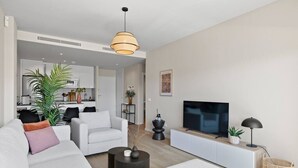 Een moderne woonkamer met een bank, salontafel, televisie en een eethoek op de achtergrond.