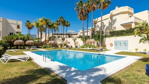 Una piscina con sillones de descanso, palmeras y un edificio de techos planos.