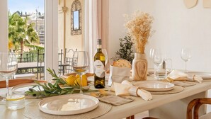 Mesa de comedor servida con platos, vasos y una botella de vino, con vista a palmeras y un balcón.