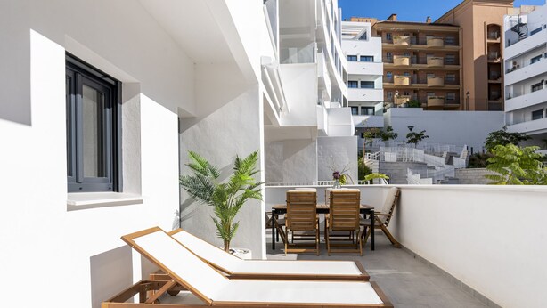 A balcony with two wooden lounge chairs, a small table, and a potted plant. - Garden View Apartment – Big Terrace (Estepona)