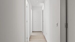 A narrow, well-lit hallway with white walls and wooden flooring, leading to a door at the end. - Garden View Apartment – Big Terrace (Estepona)