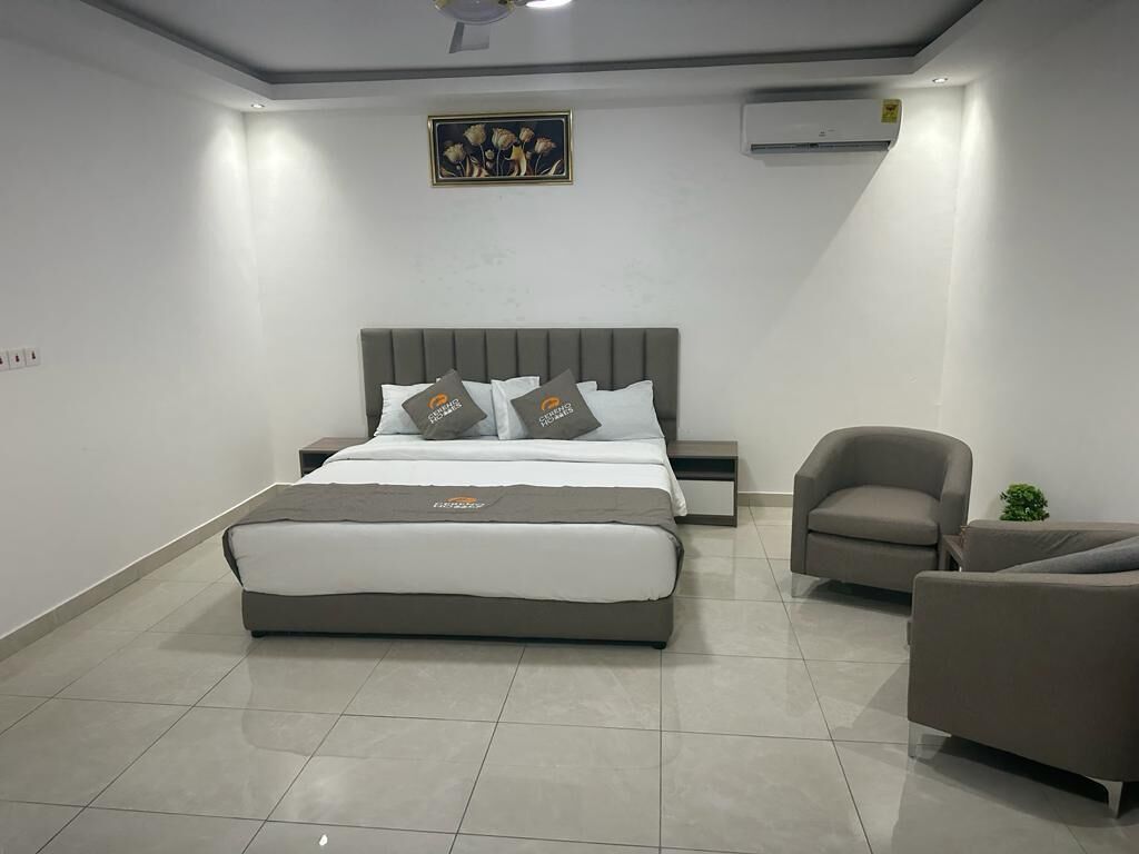 A modern bedroom with a large bed, a bedside table, a chair, and a small table with a plant.