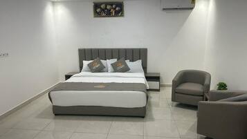 A modern bedroom with a large bed, a bedside table, a chair, and a small table with a plant.