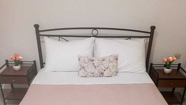 A neatly made bed with two rolled towels, a floral pillow, and two nightstands with vases of flowers. - Sweet home Lefkas (Lefkada)