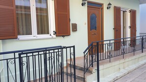 A building with a staircase, a wooden door, and a window with brown shutters. - Sweet home Lefkas (Lefkada)