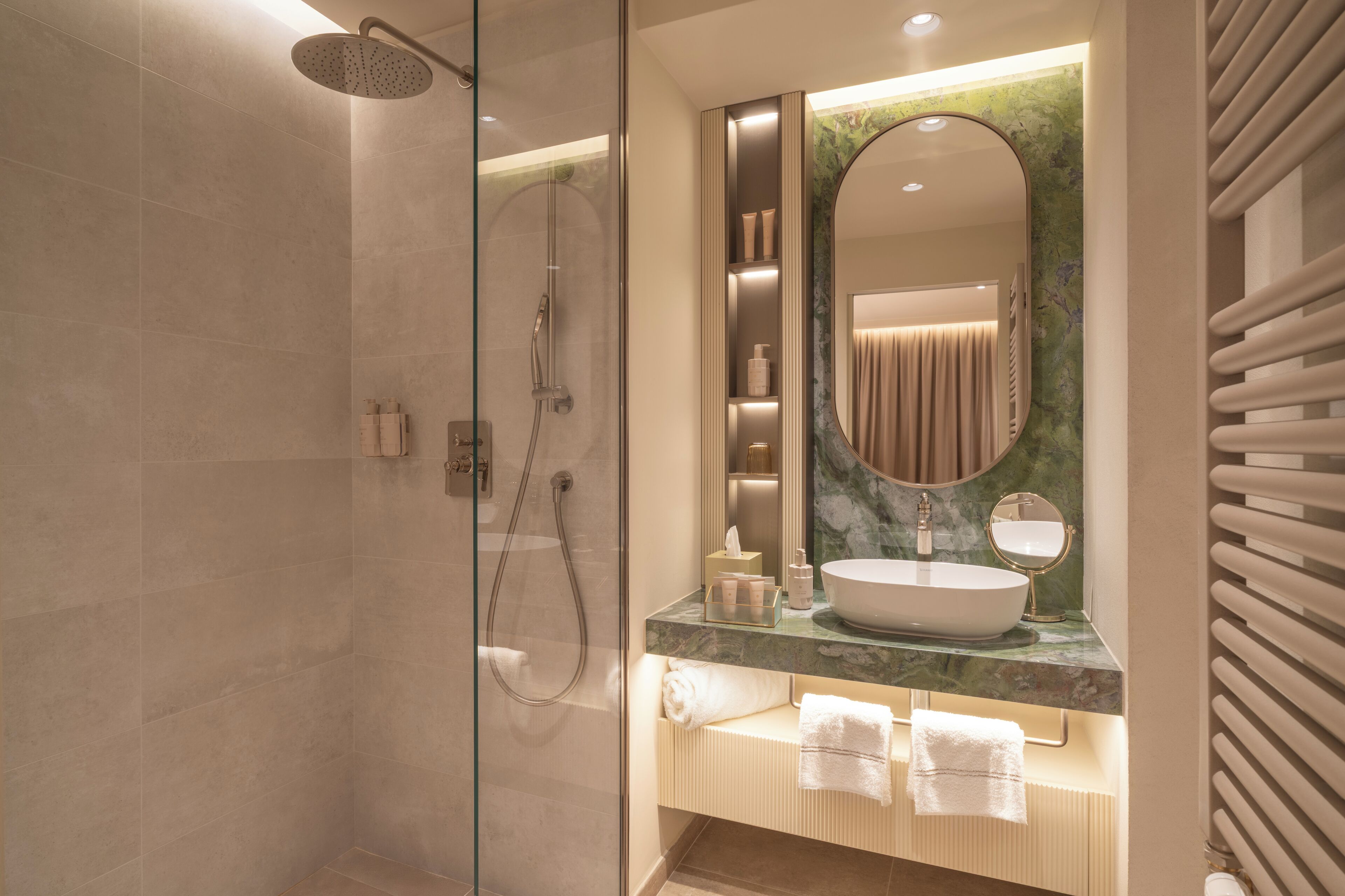 A modern bathroom with a glass-enclosed shower, a large oval mirror, and a marble countertop.