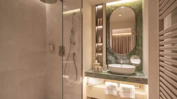A modern bathroom with a glass-enclosed shower, a large oval mirror, and a marble countertop.