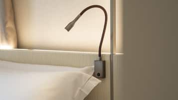 Un letto rifatto con lenzuola bianche, un comodino con una lampada e un punto luce a parete.