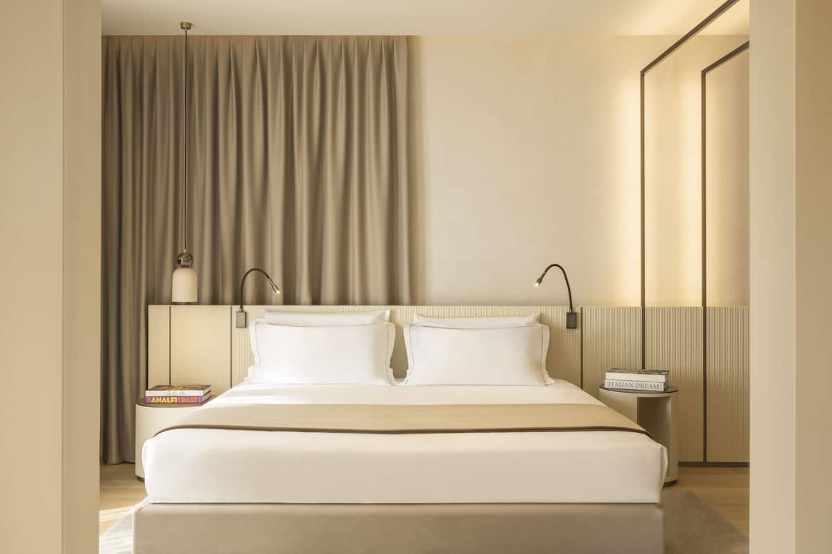 A modern hotel room with a large bed, bedside tables, and a large window with curtains.