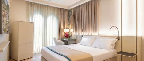 A modern hotel room with a large bed, a desk, a chair, and a wardrobe.