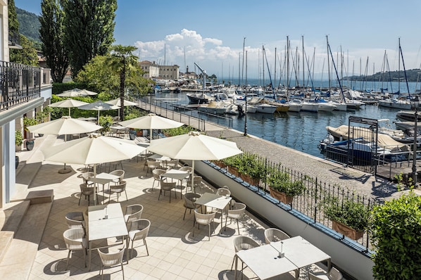 Una terraza con mobiliario exterior y vistas a un puerto deportivo con barcos.