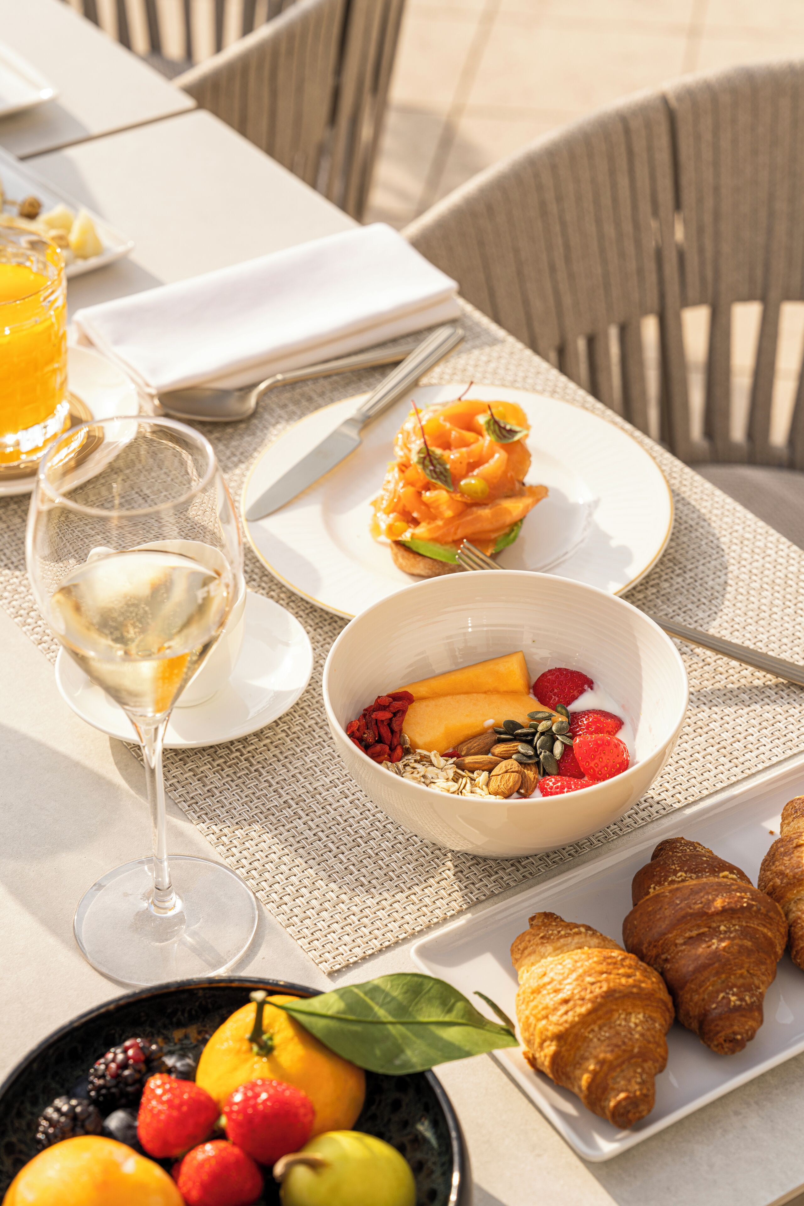 A table set with breakfast items including croissants, fruit, and a glass of white wine.