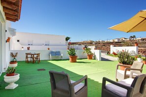 Una terraza en la azotea con mobiliario exterior, plantas en macetas y una vista despejada del paisaje circundante.