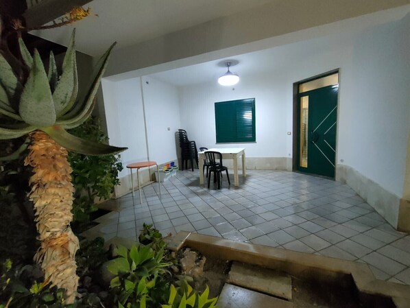 A room with a tiled floor, a table with chairs, a green door, and a window with blinds.