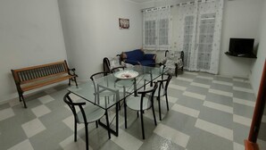 A dining area with a glass table and chairs, a bench, a sofa, and a TV on the wall. - Holiday Home 'Villetta Roby' with Private Terrace, Private Garden and Air Conditioning (Marina di Modica)
