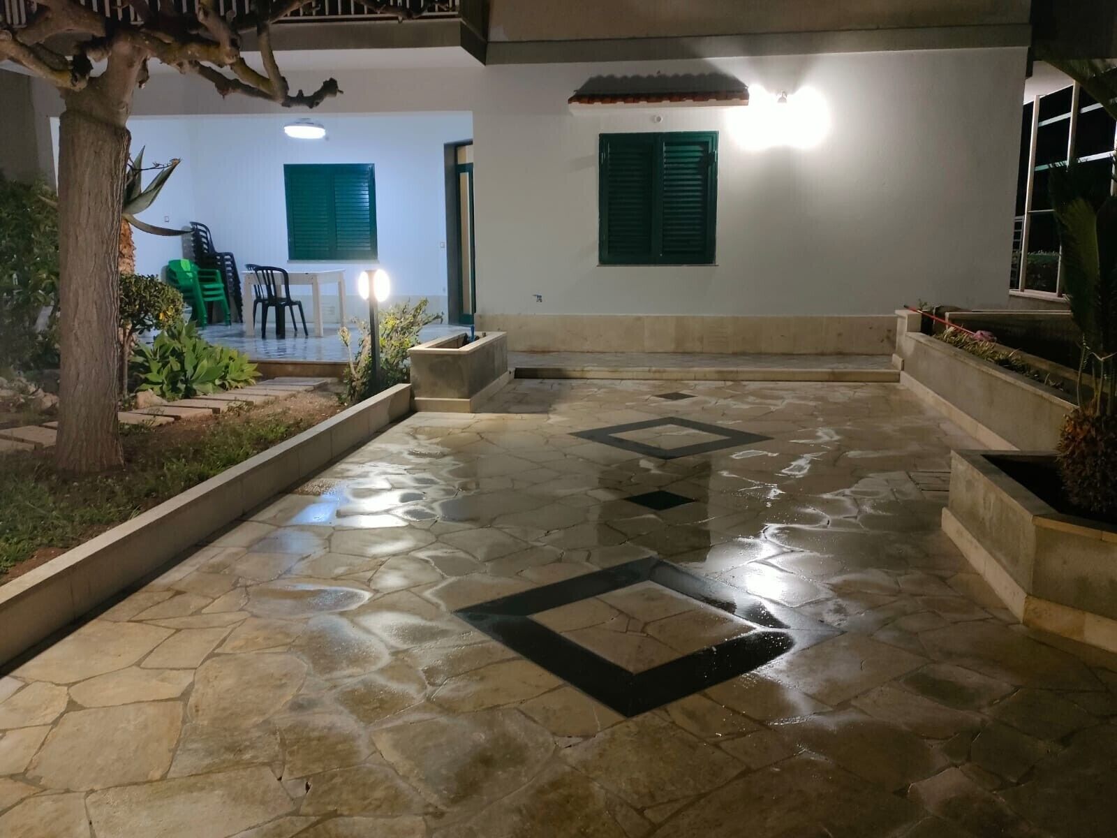 Un cortile con pavimento in pietra, un albero e un'area salotto con sedie e tavolo.