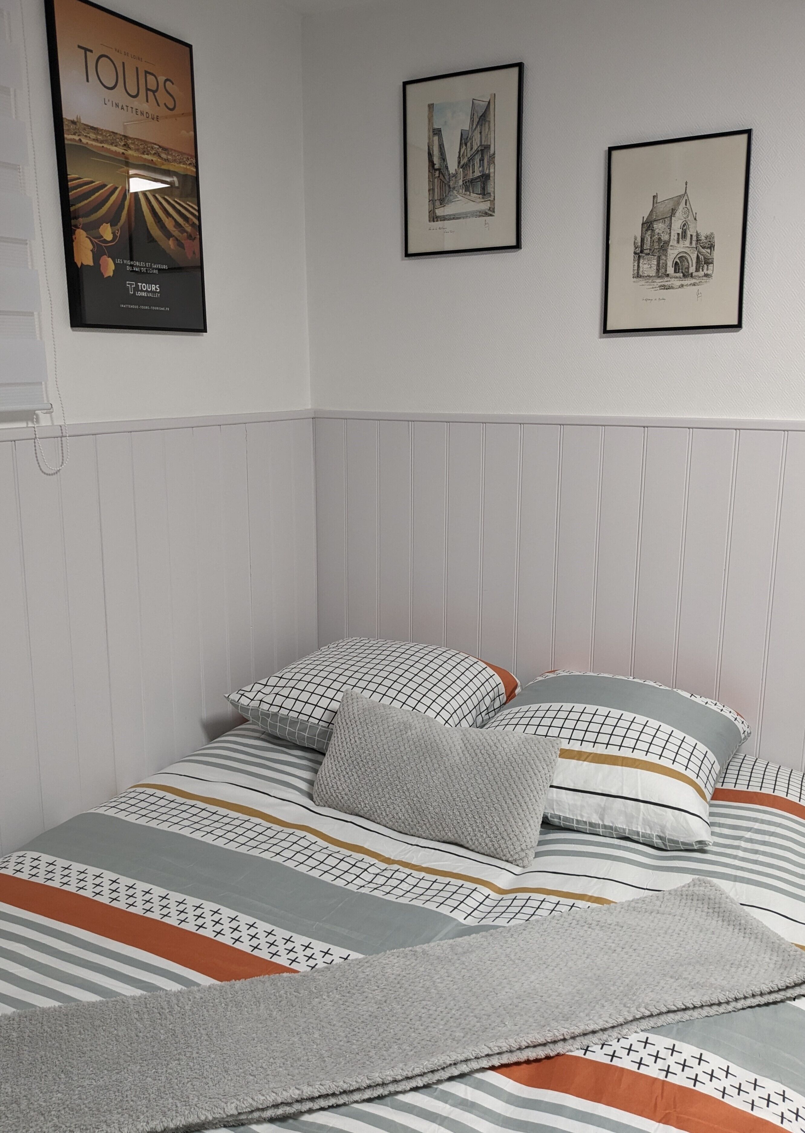 A neatly made bed with patterned bedding and pillows, a framed poster on the wall, and two framed artworks above the bed.