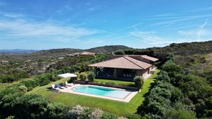 A stone house with a swimming pool, surrounded by lush greenery and hills.