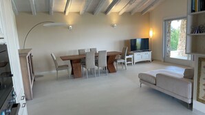 A modern living room with a dining area, a flat-screen TV, and a large window.