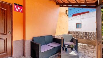 A covered outdoor seating area with a sofa and chairs, a door, and a wall with a sign.