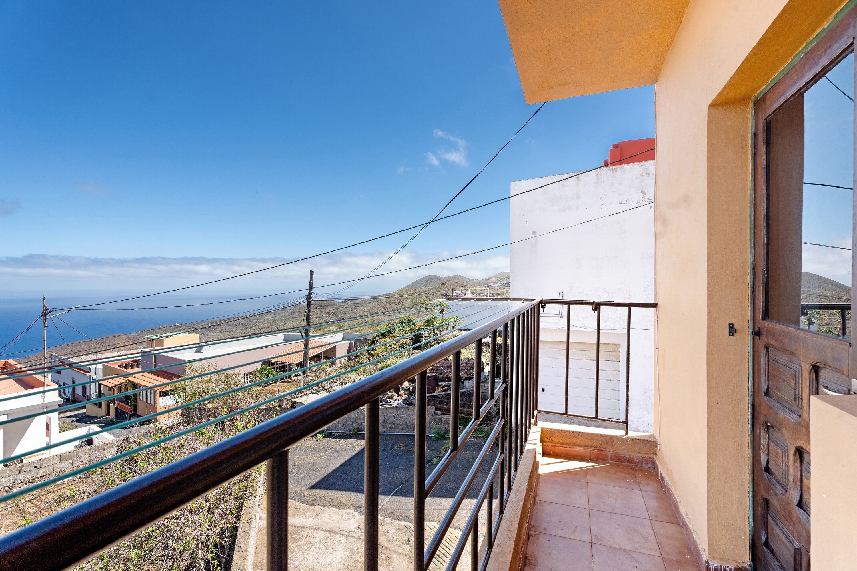 Un balcon offrant une vue sur une ville côtière, un ciel dégagé et des montagnes lointaines.