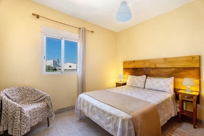 A bedroom with a bed, bedside tables, a chair, a window, and a ceiling light.