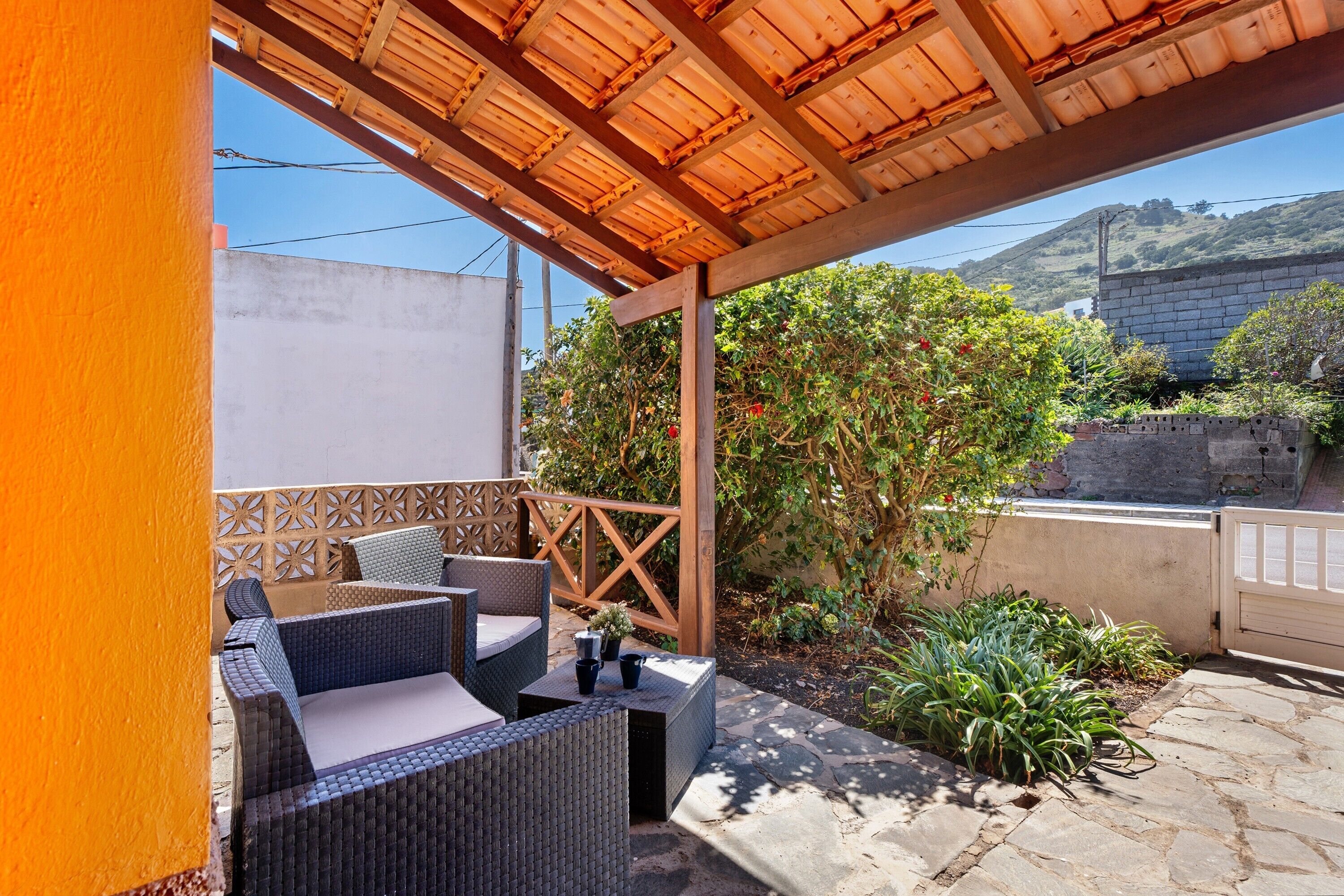Une terrasse extérieure aménagée avec des meubles en osier, une pergola en bois et une vue sur une colline.