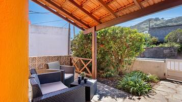Une terrasse extérieure aménagée avec des meubles en osier, une pergola en bois et une vue sur une colline.