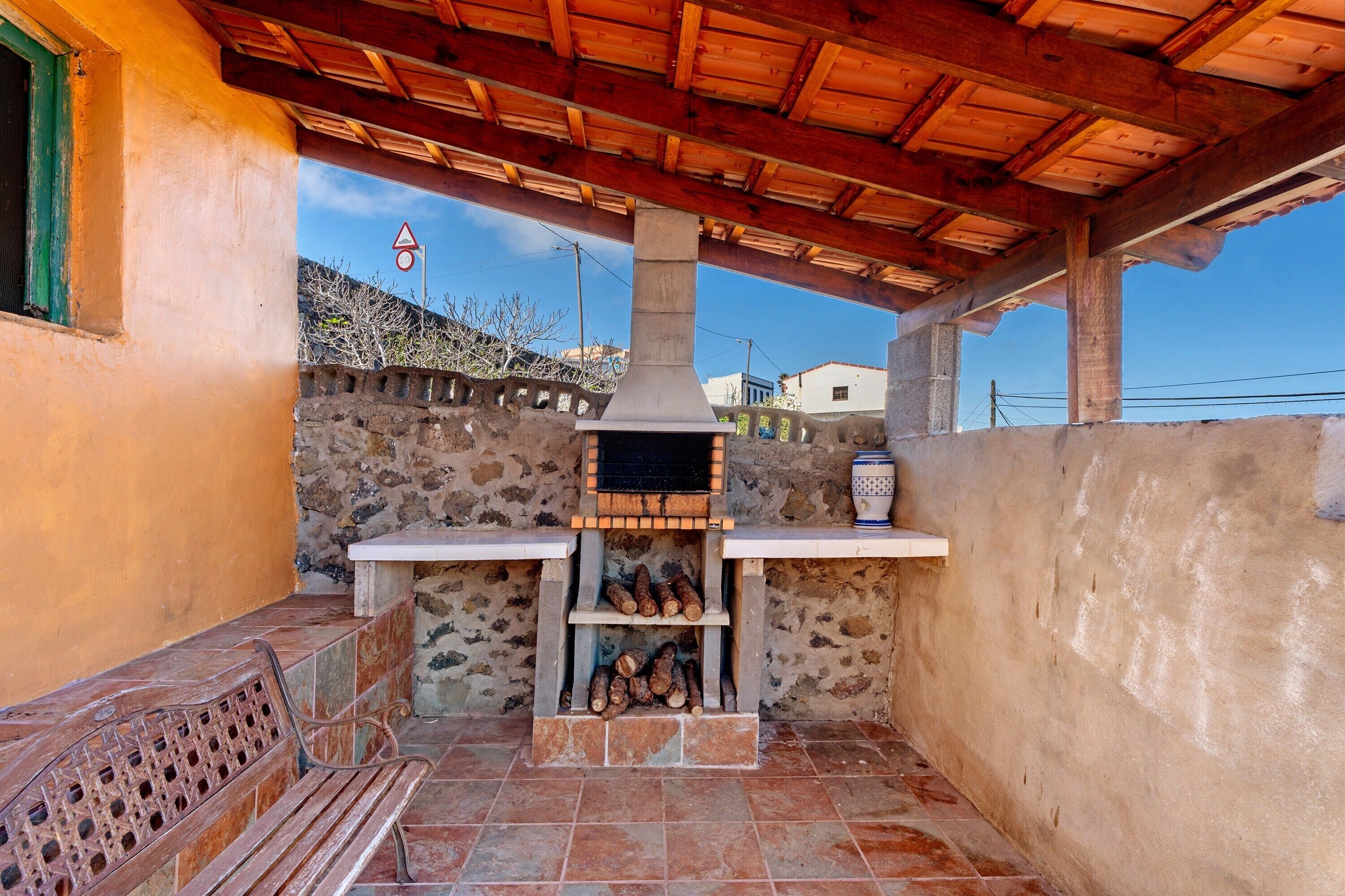 Un patio al aire libre con pared de piedra, banco de madera, chimenea y piso de baldosas.