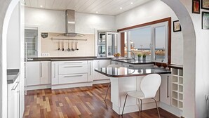 Une cuisine moderne avec des meubles blancs, un plancher en bois et une vue dégagée sur l’extérieur grâce à une arche.