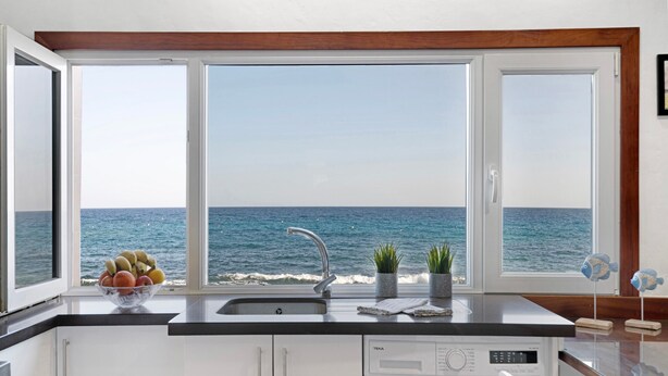 Une cuisine avec vue sur la mer, un lave-linge et un saladier de fruits sur le plan de travail.
