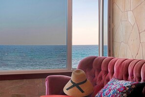 Une pièce avec une grande fenêtre donnant sur la mer, un canapé rouge et un chapeau tressé posé sur le canapé.