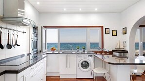 Une cuisine équipée d’un lave-linge, d’un évier et d’une fenêtre donnant sur la mer.