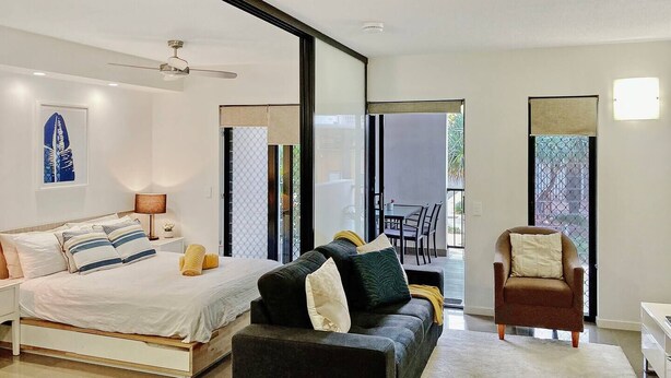 A modern bedroom with a bed, a sofa, and a chair. There is a balcony with a table and chairs. - Groovy & Cool~1Bed/1Bath/1Car~Close to everything! (Bowen Hills)