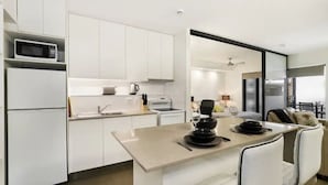 A modern kitchen with white cabinetry, a microwave, a coffee maker, and a dining area with a table and chairs. - Groovy & Cool~1Bed/1Bath/1Car~Close to everything! (Bowen Hills)