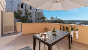 Un balcon avec une table en bois, un parasol blanc et une vue sur la ville.