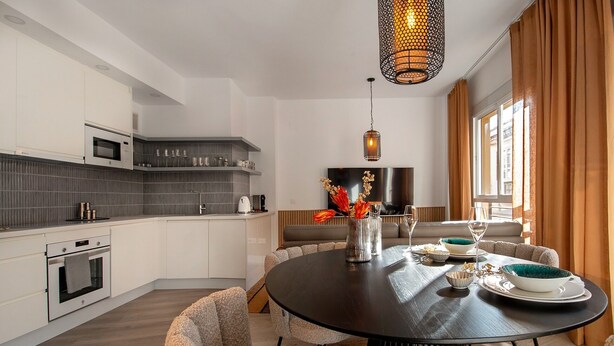 Een moderne keuken met witte kasten, een magnetron en een eethoek met een ronde tafel en stoelen.