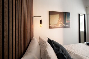 A bedroom with a wooden headboard, a single bed with pillows, a wall-mounted light, and a framed picture.