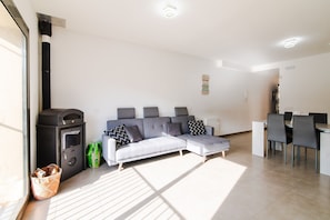 A modern living room with a grey sectional sofa, a black heater, and a dining area with a table and chairs.