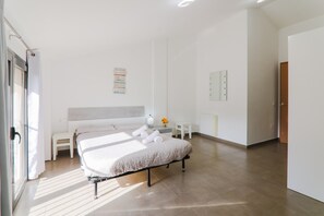 A modern bedroom with a bed, a bedside table, a small chair, a mirror, and a wall-mounted light fixture.