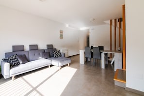A modern living room with a grey sofa, a dining table with chairs, and a staircase with wooden steps.